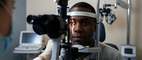 African American man receiving comprehensive eye examination from optometrist using advanced diagnostic equipment in modern clinic setting.