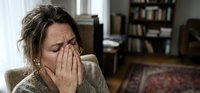 Stressed middle-aged Caucasian woman covering face with hands showing emotional distress and mental health struggles in home interior setting.