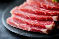 Fresh marbled raw beef slices arranged on black stone plate, close-up view showing meat texture and fat marbling pattern for premium steak preparation.