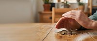 Senior hands protecting stack of coins on wooden table symbolizing retirement savings, financial security and wealth management planning.