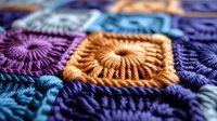 Colorful crochet granny squares in purple, orange and blue yarn creating handmade textile pattern for crafting projects and home decor applications.