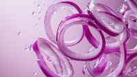 Vibrant purple onion slices with water droplets on pink background, fresh ingredient for cooking and food photography.
