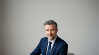 Middle-aged man with salt-and-pepper hair and facial hair wearing navy blazer and tie against neutral background for corporate portraits and business headshots.