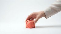 Hand reaching for red geometric origami cube on white surface, minimalist composition for business concepts and creative design projects.