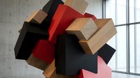 Abstract geometric sculpture with colorful wooden blocks in modern interior space with concrete wall and large window creating artistic display.