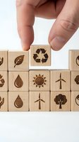 Hand placing wooden cube with recycling symbol among eco-friendly blocks featuring renewable energy and environmental icons for sustainable business concepts.
