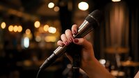 Hand holding microphone in warm concert venue with bokeh lights creating atmospheric entertainment background for live music performance and singing events.