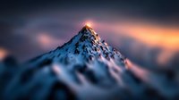 Majestic snow-capped mountain peak at sunset with dramatic orange and pink sky colors creating stunning alpine landscape for outdoor adventure content.