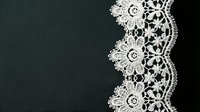 White delicate lace trim border on dark background, ornamental textile design for wedding invitations, fashion, and decorative projects.