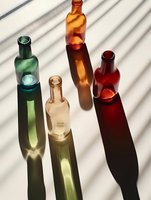 Colorful glass bottles casting long shadows on white surface with striped light pattern, creating dramatic contrast for product photography.