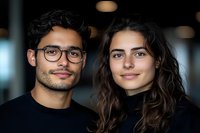 Young diverse couple smiling at camera in modern office environment. Professional millennials wearing casual black clothing for business teamwork concepts.