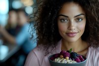 Young African American woman with natural curly hair smiling while holding bowl of fresh berries and oatmeal, wearing pink sweater. Healthy lifestyle and wellness concept.