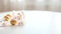 Golden wedding rings with delicate pink cherry blossoms on white surface creating romantic matrimonial scene for engagement and marriage celebrations.