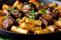 Rigatoni pasta with braised beef short ribs in rich sauce garnished with fresh herbs, served in cast iron pan. Close up view of gourmet main course.