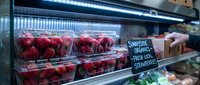 Fresh organic strawberries displayed in clear plastic containers on refrigerated grocery store shelf with price signage for healthy eating and shopping.