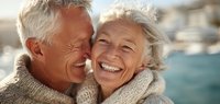 Happy senior couple laughing together outdoors in warm sweaters enjoying retirement lifestyle and romantic moments by waterfront location.