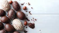 Chocolate Easter eggs decorated with sprinkles and cocoa powder on white wooden background, scattered chocolate pieces create festive composition.