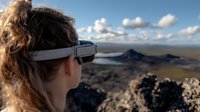 Young woman wearing VR headset gazes at dramatic mountain landscape during sunset, combining virtual reality technology with natural outdoor adventure experience.