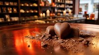 Chocolate heart-shaped confections dusted with cocoa powder on a reflective surface with warm ambient lighting, suitable for bakery, dessert, and Valentine's Day marketing materials.