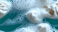 Foamy soap bubbles and white cream swirls in turquoise water creating abstract cleaning and hygiene concept for bathroom and spa designs.