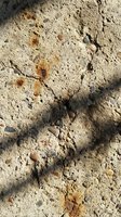 Cracked dry earth surface with scattered pebbles and rust-colored stains, showing weathered ground texture with natural fissures and erosion patterns.