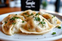 Homemade dumplings garnished with fresh herbs and black pepper on white plate, close up view of traditional Asian cuisine with delicate folded wrappers.