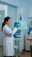 Female doctor in white coat explaining holographic lung scan to patient in modern medical clinic with advanced digital technology.