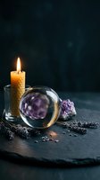 Crystal ball with burning candle and amethyst stones on dark slate surface with dried lavender sprigs creating mystical fortune telling atmosphere.