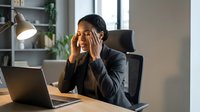 Stressed African American businesswoman experiencing headache while working on laptop in modern office environment during busy workday.