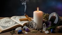 Mystical altar setup with burning candle, open spell book, pentagram pendant, crystals, herbs and incense smoke for witchcraft rituals and spiritual practices.