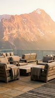 Luxury mountain terrace with wooden furniture and cushions overlooking golden-hour alpine peaks, perfect for hospitality and travel marketing.