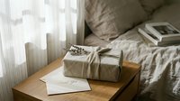 Wrapped linen gift box with dried lavender and thank you card on wooden nightstand in cozy bedroom with soft natural light.