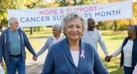 Senior Hispanic woman with pink ribbon leading cancer support group holding hands in park during awareness month fundraising event.