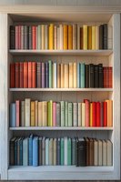 Colorful vintage books arranged on white wooden shelves creating rainbow pattern. Collection of old hardcover volumes in pastel and bright spines forms aesthetic display.