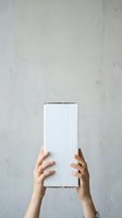 Two hands holding white corrugated cardboard box against concrete wall background for product packaging, shipping, delivery, and unboxing concepts.
