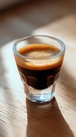 Fresh espresso shot with golden crema in glass cup on wooden surface, dramatic natural lighting casting soft shadows, close-up view for coffee menu and cafe promotion.