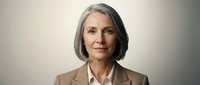 Professional mature Caucasian businesswoman with gray hair in beige suit jacket smiling confidently against neutral background for corporate presentations.