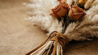 Dried rose buds and pampas grass bouquet tied with leather cord on rustic burlap, boho wedding decor and autumn arrangement.