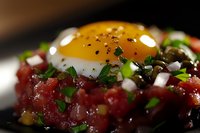 Raw tuna tartare topped with sunny side up quail egg, garnished with fresh chives and black pepper, served as gourmet appetizer on dark plate.