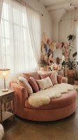 Round pink velvet sofa with decorative pillows in modern bedroom interior with natural light from window, potted plants, and contemporary home decor styling.