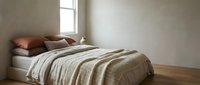 Cozy bedroom interior with unmade bed featuring neutral bedding, wooden floor, and natural light from window for home decor design.