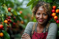 Young African American female farmer in red apron smiling confidently among ripe coffee cherries on plantation, sustainable agriculture and organic farming concept.