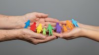 Colorful paper cutout figures representing diverse community held protectively between caring hands symbolizing unity, support and social connection.