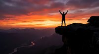 Silhouette of person with raised arms celebrating success on mountain cliff edge during dramatic orange sunset sky over valley landscape for motivation concepts.