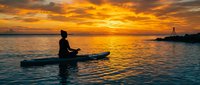 Man kayaking at sunset with golden sky reflecting on calm ocean water creating peaceful evening seascape for outdoor recreation and water sports activities.