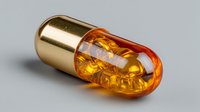 Golden capsule pill with transparent amber shell containing yellow liquid oil supplement on white background isolated for pharmaceutical design.