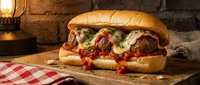 Meatball sandwich with melted cheese and tomato sauce on wooden board, rustic setting with checkered cloth and warm lighting for food photography.