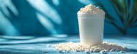 Creamy protein powder in white scoop surrounded by scattered supplement on blue background with tropical plant shadow.