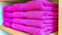 Stack of folded bright pink towels neatly arranged on wooden shelf for bathroom decor and home organization storage solutions.