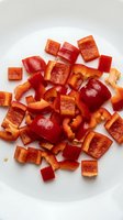 Fresh red bell pepper pieces chopped and diced on white background, ready for cooking and meal preparation in kitchen.